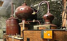 Copper distillation stills in a brick-walled distillery, connected by copper pipes.